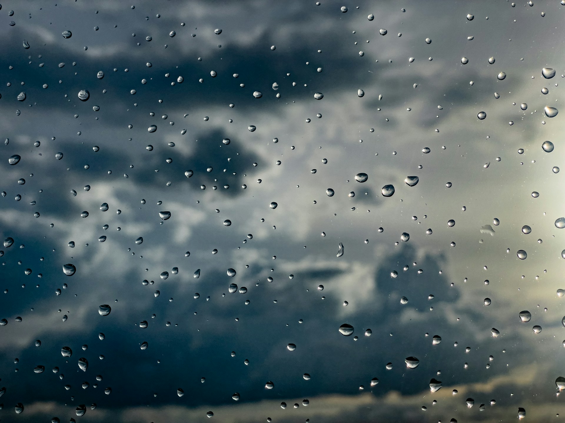 Rain drops on a window with a cloudy sky behind it, illustrating the start of wet season for home cleaning in Clermont, FL