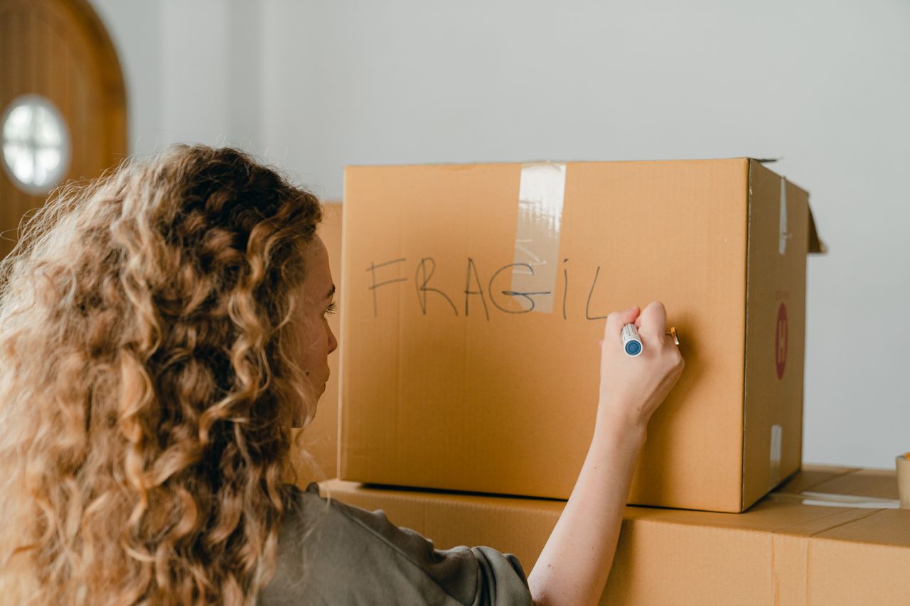 A female presenting person writing Fragile on a moving box