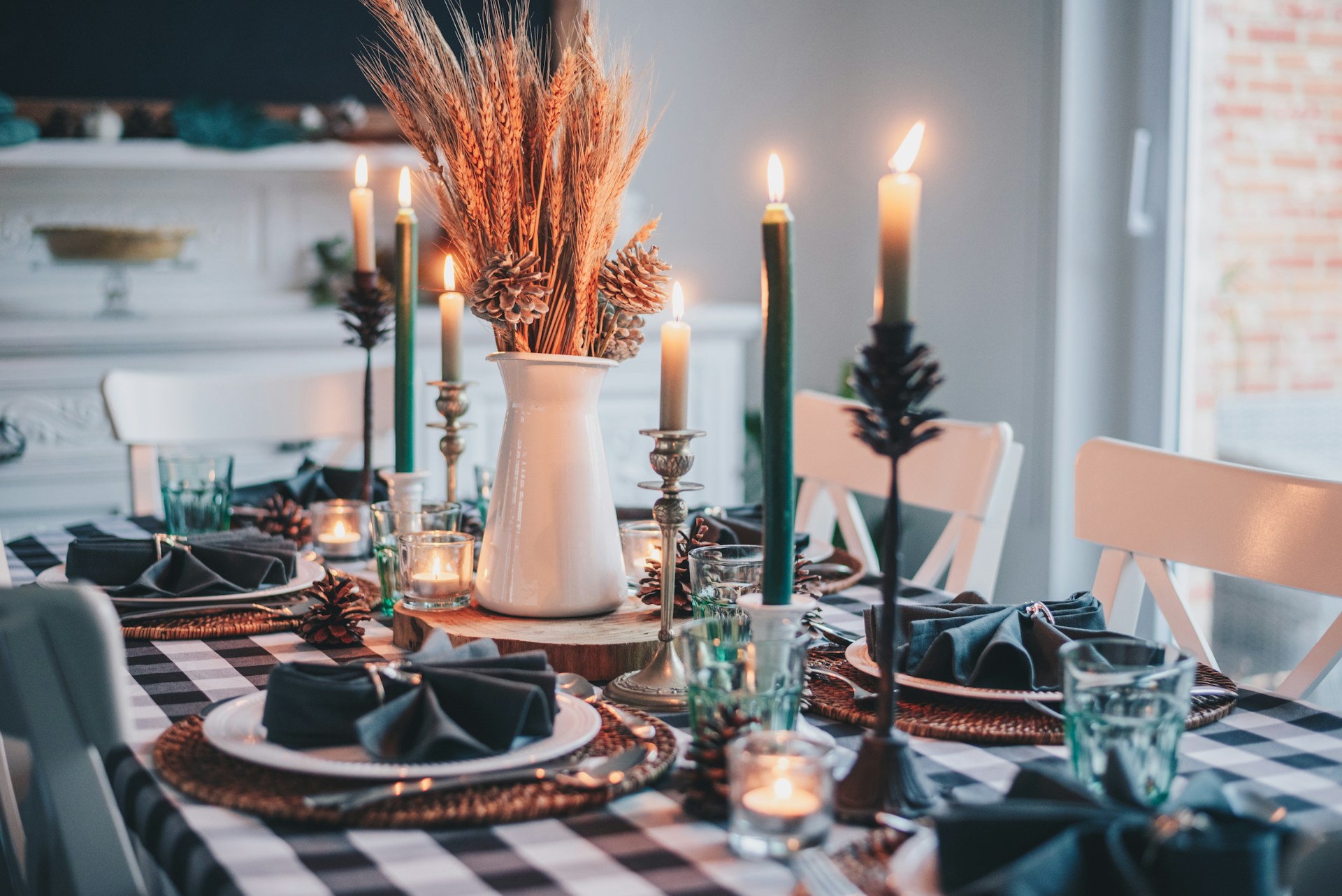 table set for the holidays: checkered table cloth with full formal place settings, lit candles and pampas grass